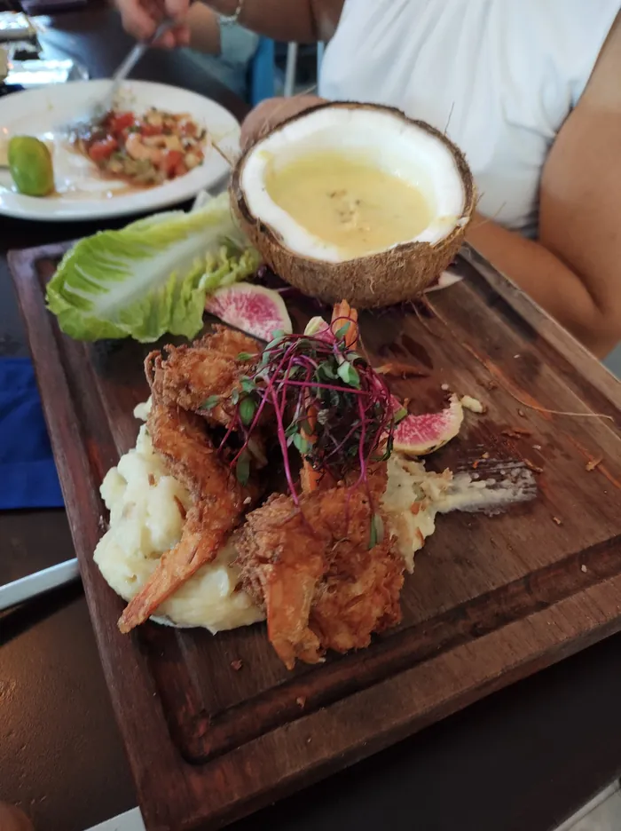 Camarones al coco sobre tabla de madera, con salsa servida en medio coco