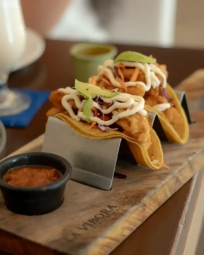 Dos tacos capeados con aderezo y aguacate sobre una tabla de madera con La Víbora grabado